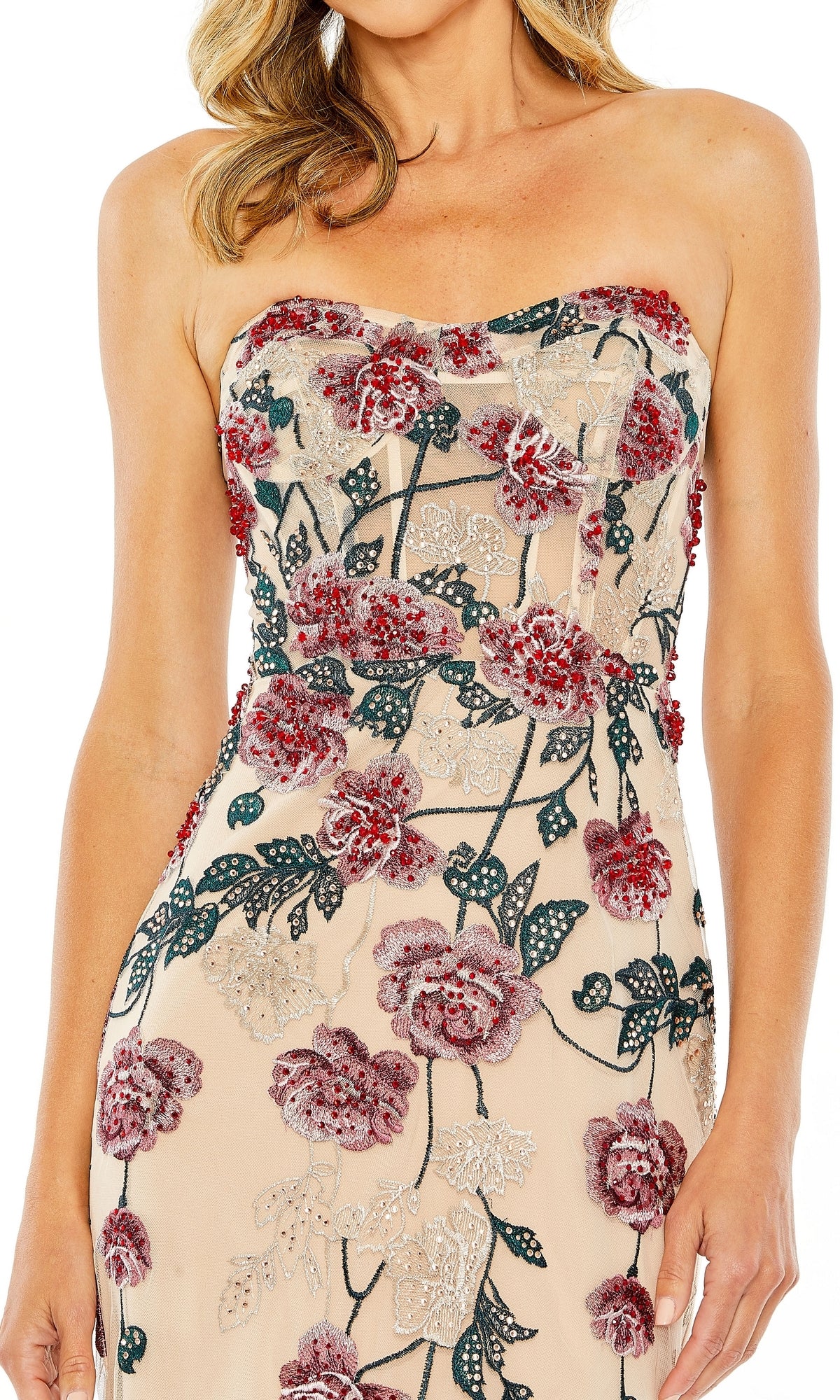 A woman poses confidently with one hand on her hip, wearing the beige Long Formal Dress 20581 by Mac Duggal with red and green floral embroidery.